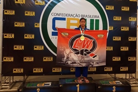 Aluna exibe bandeira do projeto e a medalha de Campeã Brasileira de Jiu Jitsu